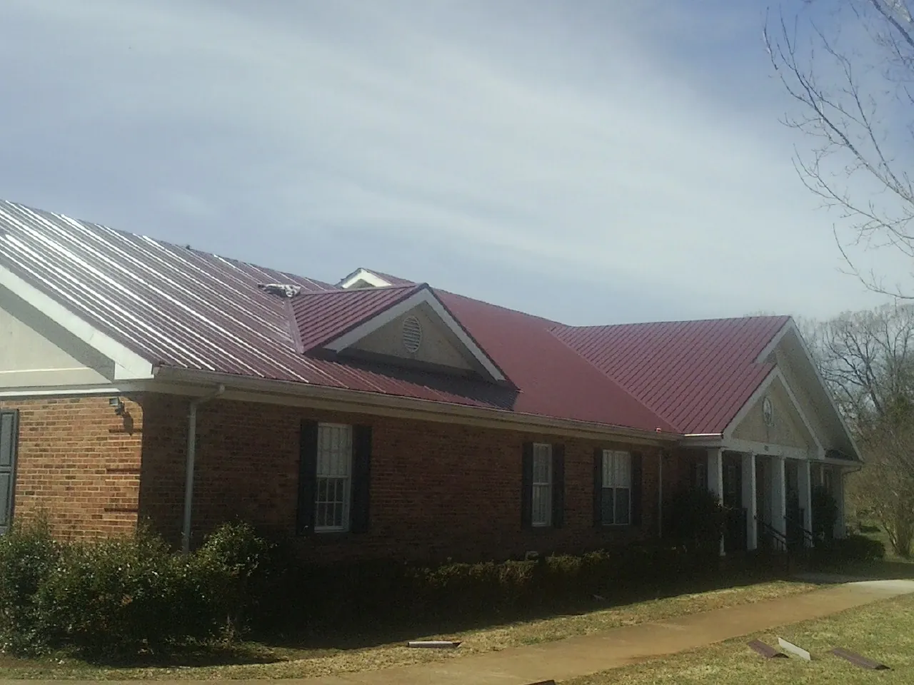 Red metal roof with gabled entries on a long brick building, from a Hail Damage Roof Repair job in Berne