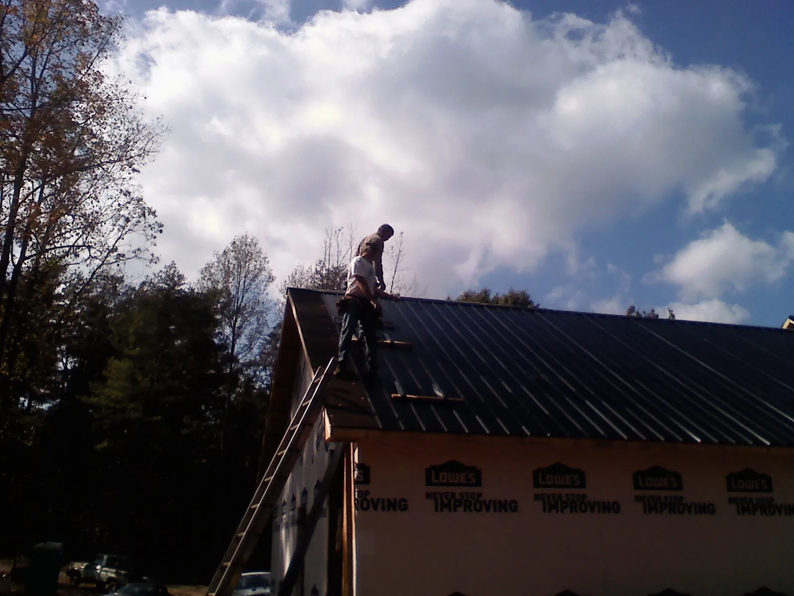 Roofer fastening dark metal panels high against a cloudy sky, from a Roof Inspection job in Berne